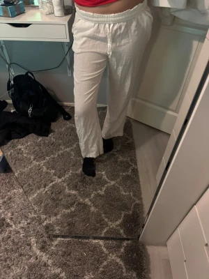 Vita linnebyxor med snörning - Säljer ett par vita linnebyxor med avslappnad passform och snörning i midjan. Byxorna har elastisk midja och raka ben, vilket ger en chill och luftig vibe. Perfekta för varma dagar eller när du vill ha det bekvämt. Fickor bak för extra funktion.