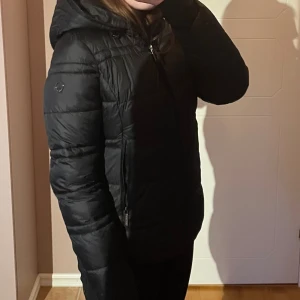 Micheal Kors jacka - Säljer en svart pufferjacka från micheal kors med huva och två dragkedjor. Jackan har quiltad design, dragkedja framtill och två fickor med dragkedja. Perfekt för kalla dagar och har en stilren look som funkar till det mesta.