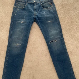 Replay Anbass jeans - Säljer ett par Replay Anbass jeans i klassisk blå tvätt med slitningar och trasiga detaljer på benen. Knappt använda över huvudtaget. Storlek 32/32