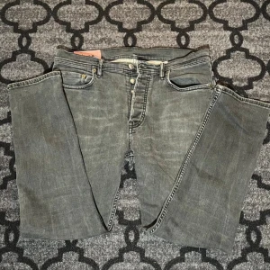 Grå jeans från Acne Studios Blå Konst - Säljer ett par grå jeans från Acne Studios Blå Konst, modell med klassisk femficksdesign och raka ben. Jeansen har en snygg tvättad look och är tillverkade i bomull. Perfekta för dig som gillar stilrena och trendiga byxor.