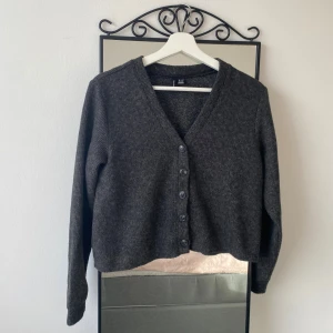 Mörkgrå kofta  - Mysig mörkgrå kofta med v-ringning. Koftan har långa ärmar och knäpps med knappar framtill. Perfekt att slänga över en t-shirt eller linne för en chill look.