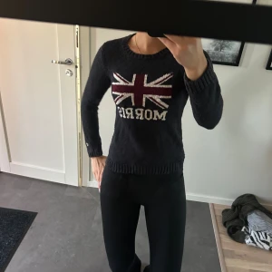 Mörkblå stickad tröja Morris Lady - Mörkblå stickad tröja från Morris Lady med Union Jack-flagga och vit text framtill. Tröjan har rund halsringning, ribbade muddar och lång ärm. Bra skick och storlek xs.