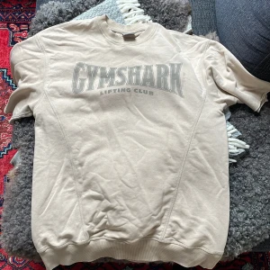 Beige Gymshark sweatshirt S - Säljer en beige sweatshirt från Gymshark i storlek S med stort tryck 'GYMSHARK Lifting Club' på bröstet. Tröjan har rund hals, ribbade muddar och är tillverkad i mjuk bomull. Perfekt för gymmet eller chill dagar.