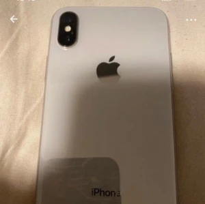 iPhone XS - Snygg iPhone XS i silver med dubbla bakre kameror och elegant glasbaksida. Skärmen är stor och utan synliga sprickor. Telefonen ser ut att vara i gott skick utan tydliga repor eller skador. Perfekt för dig som vill ha en kraftfull och stilren smartphone.