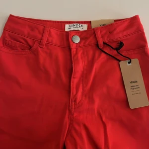 Röda wide leg byxor från Lindex - Snygga röda byxor från Lindex, modell Viola med extra vida ben och hög midja. Klassisk femficksdesign, knapp och dragkedja framtill. Tillverkade i bomull för en skön känsla och cool look. Perfekta för dig som gillar statement-plagg.