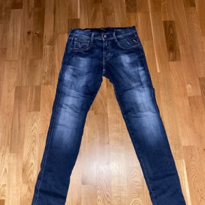 Replay Anbass jeans blå storlek  - Snygga Replay Anbass jeans i mörkblå tvätt med slitningar och klassiska fem fickor. Slim passform och raka ben, med detaljerade sömmar och dragkedja. Perfekt för dig som gillar stilrena och moderna jeans.