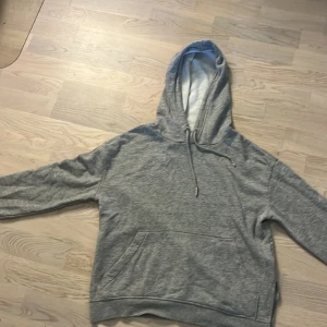 Grå hoodie från H&M Divided XS - Mysig grå hoodie från H&M Divided i storlek XS. Tröjan har huva med snörning, magficka och mjukt fleecefoder på insidan. Perfekt för chill dagar eller när du vill vara extra bekväm. Klassisk modell med ribbade muddar vid ärmslut och nederkant.