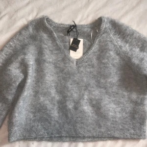 Ljusgrå stickad v-ringad tröja från bikbok  - Supermjuk ljusgrå stickad tröja från bikbok med v-ringning och lång ärm. Tröjan har en fluffig känsla och ribbade muddar vid ärmslut och nederkant. 