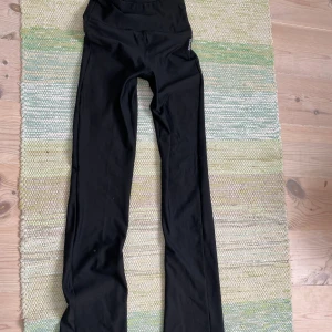 Svarta bootcut träningsbyxor från SOC - Svarta träningsbyxor från SOC med bootcut-snitt och hög midja. Stretchigt material som sitter skönt och följer kroppen. Perfekta för gymmet eller yoga. Diskret logga på höften och klassisk look.