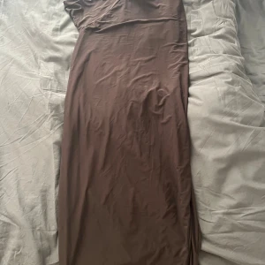 Brun one shoulder långklänning Boohoo - Säljer en snygg brun långklänning från Boohoo med one shoulder-design. Klänningen har en slät, figurnära passform och är tillverkad i ett mjukt, stretchigt material som ger en stilren look. Perfekt för dig som vill sticka ut med en trendig och elegant stil.