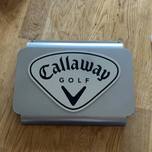 Callaway Golf skylt - Snygg Callaway Golf-skylt i metall, perfekt för golfentusiasten. Skylten är i gott skick med tydlig logotyp och inga större repor eller skador. Passar utmärkt som dekoration i garage, golfklubb eller hemmakontor.
