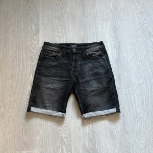 Svarta jeansshorts Jack & Jones - Snygga svarta jeansshorts från Jack & Jones med klassisk femficksdesign och uppvikta benslut. Shortsen har en normal passform och är tillverkade i bomull med lite stretch för extra komfort. Perfekta för en chill sommarlook.