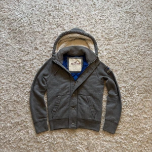 Grå hoodie/cardigan från hollister - Sjukt snygg o limiterad hoodie/cardigan från hollister. Den är grå med fodrad luva och insida som gör den extra varm vilket passar perfekt nu till hösten/vintern. Mycket bra skick, hittade två minimala fläckar som syns på de två sista bilderna, men det är verkligen inget man lägger märke till annars. Storlek S, tveka inte i skriva vid frågor!