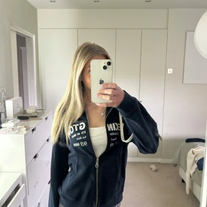 Mörkblå hoodie från lexington med tryck - Säljer en mörkblå hoodie från lexington med vitt tryck på bröstet och dragkedja framtill. Tröjan har huva med vita snören och två fickor. Perfekt för dig som gillar en sportig och avslappnad stil.