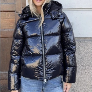 Svart glansig pufferjacka från Nelly - Svart pufferjacka från Nelly med glansig finish och stor huva, st S. Använd fåtal gånger (max 10) och ser ut som ny💕nypris 799kr