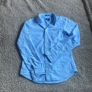 Ljusblå skjorta från GANT  - Snygg ljusblå skjorta från GANT i storlek XS MEN PASSAR S BÄTTRE. Klassisk modell med knappar hela vägen, krage och broderad logga på bröstet. Skjortan är tillverkad i mjuk bomull och har lång ärm. Perfekt för dig som gillar stilrena och tidlösa plagg. AS fet skjorta du kan ha till alla möjliga tillfällen! Passar mer S som sagt! Fler frågor? Hojta till så löser vi det! MVH SWISSWEAR 🇨🇭🍾🏔️❤️