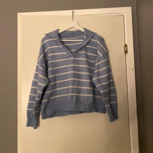 Blåvit randig stickad tröja med krage - Mysig stickad tröja i ljusblått med vita ränder och bred krage. Tröjan har v-ringning, ribbade muddar och en loose passform. Perfekt för lager-på-lager och chill dagar. Snygg till jeans eller kjol.Passar perfekt nu till hösten 💙
