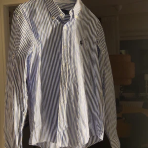 Randig skjorta från Ralph Lauren M - |Pris kan självklart diskuteras| Klassisk blåvit randig skjorta från Ralph Lauren i modellen Classic Fit. Skjortan har lång ärm, knappar framtill och ikonisk broderad logga på bröstet. Tillverkad i mjuk bomull och passar perfekt till en clean och stilren look.