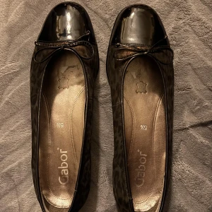 Leopardmönstrade ballerinaskor Gabor - Snygga ballerinaskor från Gabor med leopardmönster i mörkbruna och svarta toner. Skorna har rund tå med lackad svart topp och en söt rosett framtill. Platt sula och insida i skinn för extra komfort. Perfekta för dig som gillar djurmönster och stilrena detaljer. Mycket god skick nästan som nya original pris 1400kr mitt pris 500kr 