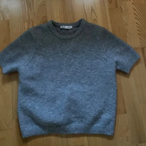 Grå stickad tröja från Zara - Mysig grå stickad tröja från Zara med korta ärmar och rund hals. I väldigt fint skick och bara använd några gånger. I storlek L men väldigt liten i storleken så sitter mer som en XS/S. 