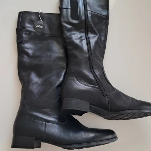 Svarta skinnstövlar från Gabor - Helt nya svarta stövlar från Gabor i mjukt skinn med låg klack och rund tå. Dragkedja på insidan för enkel påtagning och robust sula med bra grepp. Perfekta för dig som vill ha en klassisk look med bekväm passform.