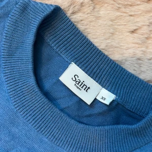 Blå stickad tröja från Saint Tropez - Säljer en blå stickad tröja från Saint Tropez i storlek XS. Tröjan har korta ärmar med lätt puff vid axlarna och bred ribbad kant vid halsringningen och nederkanten. Perfekt för dig som gillar en enkel men snygg look.