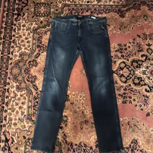 Replay Anbass jeans mörkblå 34/32  - Säljer ett par Replay Anbass jeans i mörkblå tvätt med snygga slitningar. Klassisk femficksmodell med smal passform och raka ben. Jeansen har detaljerade sömmar och Replay-logga på fickan. Perfekta för dig som gillar stilrena och moderna jeans. Midja 43cm längd 97cm (49)