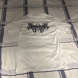 Vit t-shirt med svart tryck - Vit t-shirt med korta ärmar och ett svart grafiskt tryck på bröstet. T-shirten har en klassisk passform och rund halsringning. Materialet ser ut att vara mjukt och lätt, perfekt för en avslappnad stil. Används till någon slags träning denna är commpressed och är i storlek s/m