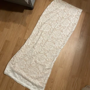 Vit långkjol med blommigt mönster Mussera - Supersnygg långkjol från Mussera i vit spets med blommigt mönster. Kjolen är gjord i polyester och har en elegant, rak form som ger en stilren vibe. Perfekt för dig som gillar romantiska detaljer och vill sticka ut med en unik look. Storlek L men sitter mer som S