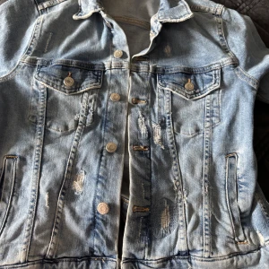 Ljusblå jeansjacka från &Denim - Säljer en ljusblå jeansjacka från &Denim i storlek 44. Jackan har slitna detaljer, klassisk krage, två bröstfickor med knappar och sidofickor. Den är tillverkad i jeansmaterial och har en cool, avslappnad vibe med knappstängning framtill.
