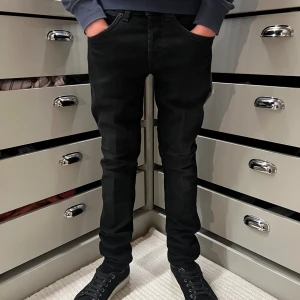 Svarta Dondup jeans slim fit George - Svarta jeans från Dondup i slim fit. Byxorna har en rak siluett, diskreta sömmar och är tillverkade i ett mjukt bomullsmaterial med stretch. Perfekta för dig som gillar en stilren och modern look.          I modellen George.                                             Skick= helt nya med tags nypris=3000