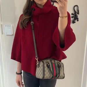 Röd poncho från Zara Woman - Snygg röd poncho från Zara Woman med hög krage och stor knappdetalj. Modellen är loose fit med vida trekvartsärmar och rak siluett. Perfekt för dig som vill ha en statementjacka i ullblandning till höst och vinter.