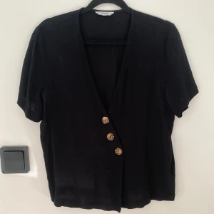 Svart blus med knappar från Envii - Svart blus från Envii med korta ärmar och v-ringning. 