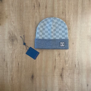Mössa louis vuitton grå -  Stylish Louis Vuitton beanie in a grey checkered pattern. Features the iconic LV logo and comes with original tag.  ⭐️ Condition: 10/10 🎨 Color: Grey 📦 Fast and careful shipping