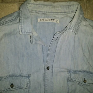 Junkyard Jeans skjorta - Fin jeansskjorta från Junkyards egna märke. Sitter perfekt både uppknäppt med något under eller knäppt hela vägen upp. Storlek XL.