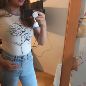  - En jättefin och bekväm T-shirt från H&M. Den har en jättefin ros mitt på och helt vit där bak. De blåa ränderna på ärmarna och halsen gör tröja så fin! Den är knappt använd och säljs för att den inte kommer till användning. 