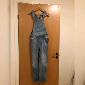 - Snygg bib (hängselbyxa) i jeans från Dr Denim. Väldigt sparsamt använda, max 3 gånger. Vet inte exakt vilken storlek dessa är men de går att ställa ut lite med extra knapphål i midjesektionen. På mig som är 92 runt gumpen och 84 i höft sitter de bra! 