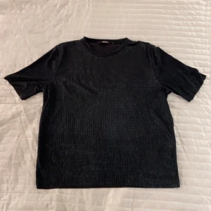 Svart glansig topp - Svart glänsande topp i fint material från Bikbok, strl S. Tröjan är i ett ”randigt” och finare material som glänser/glittrar i ljus. Aldrig använd.