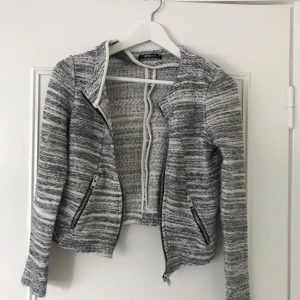  - Grå/vit kofta med dragkedja och fickor.