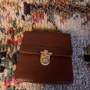 Vintageväska - brun med ängel - ✨👼✨ Vintageväska ✨👼✨ Fin i boxig modell med flera fack inuti = lagom stor men samtidigt rymlig! Axelrem/kedja 107cm. I ett fint skick, små tecken på användning finns. Skinnimitation. Mått: 17 x 18 x 6 cm. Frakt tillkommer på 63 kr.