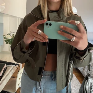 Militärgrön höstjacka - Otroligt cool militärfärgad höstjacka. Fina spännen på armarna (sista bilden) samt även på axlarna. Använd en gång så i princip nyskick.