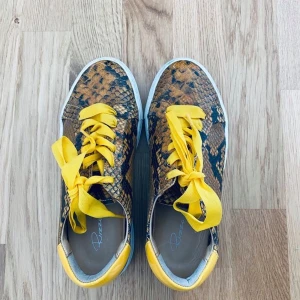 Sneakers från Rizzo  - Sneakers i skinn med gula detaljer. Skorna är i väldigt bra skick och sköna att gå i. Både roliga till fest & vardags. 