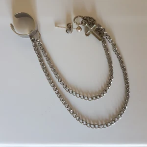 Örhänge med kors, kedja & klämma - Örhänge med ett kors, som är kopplad på två kedjor som leder till en klämma som du klämmer fast runt ytterörat. Finns för avhämtning i Malmö, alt kan skickas (mot att köparen betalar frakten). Betalning via swish.