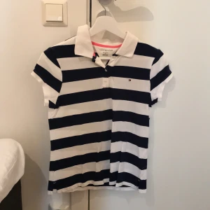Piké Tommy Hilfiger - Knappt använd piké från Tommy Hilfiger. Storlek 16 år. Vit och marinblå randig. Frakt tillkommer