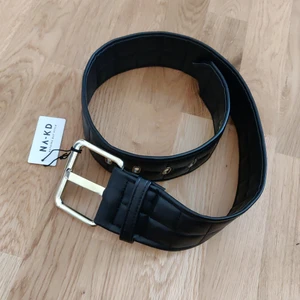 Svart brett skärp Na-kd  - Svart brett skärp med gulddetaljer från Na-kd. Oanvänd så alla lapparna finns kvar. Fraktkostnaden tillkommer.