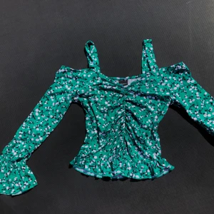 blommig off-shoulder ruched crop-top  - 💕 en grön off-shoulder crop-top med blommor, ruched detalj nerför magen samt volanger. endast använts ett få tal gånger, bra skick, mycket bekväm samt strechbar vid midjan & ärmarna. frakt kostnad tillkommer