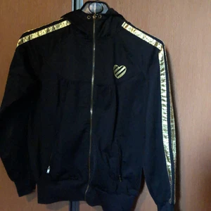 Bik Bok - Svart vct luvtröja med guld dekorationer. Snygg skärning vid axelparti. Fickor med dragkedja. Tröjan är i gott skick. Köpare betalar frakt 