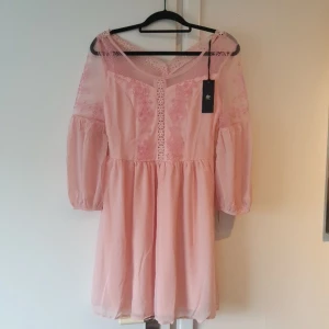 Romantisk klänning - Helt ny, oanvänd rosa klänning. Denna är jättefin med mycket fina detaljer. Puffärm. Det är "dubbelt " lager kjolar ett tunnare tyg utanpå och en "underkjol". Klänningen är köpt i M/L jag skulle säga att den är mer M. 