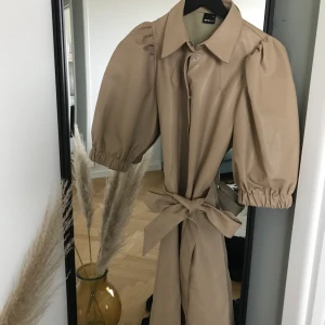 Klänning från Gina Tricot - Beige klänning i strlk M med ett bälte som kan knytas runt midjan. Köpt denna sommar. 