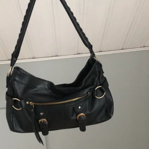 Svart handväska  - Väskan är köpt begagnad och använt ett antal gånger men nu har jag börjat tröttna på den. ” flärpen ” som suttit på dragkedjan är borta ( se bild 3)  men det har funkat lika bra för mig ändå. Frakten är inkluderad i priset.✨